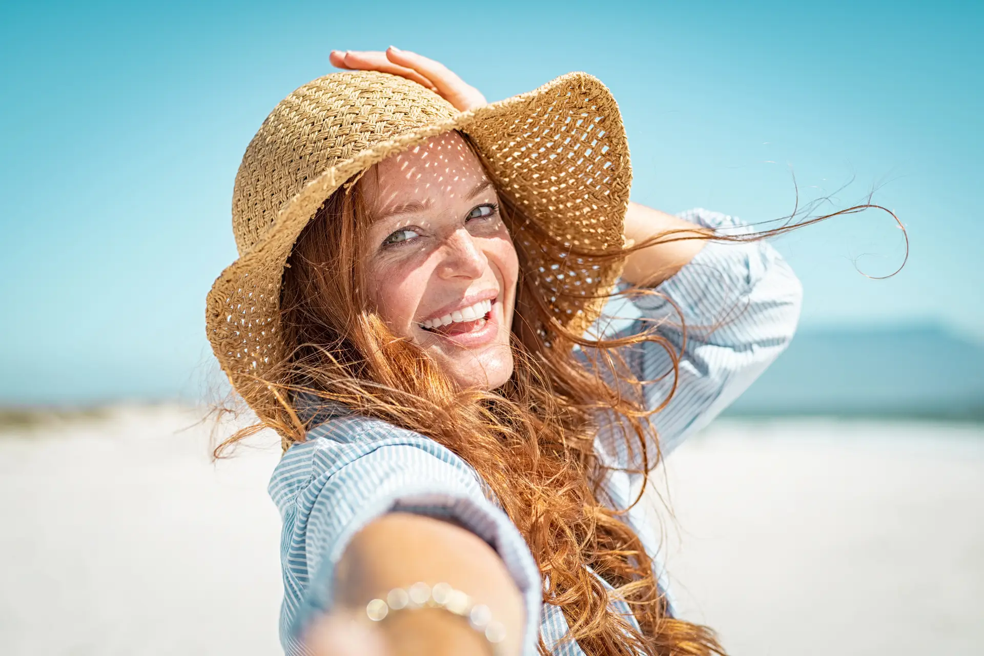 Young woman wearing straw hat, smiling in the sunshine.