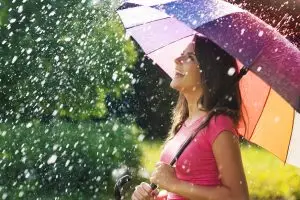 Woman holding colorful umbrella in the rain, and smiling.